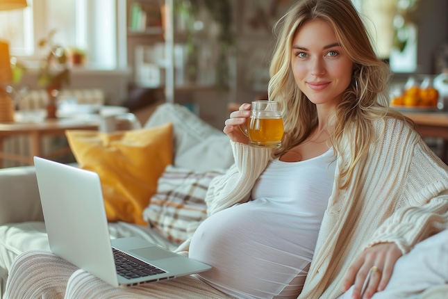 pregnant-woman-sits-sofa-drinks-tea-laptop-sofa-good-daylight